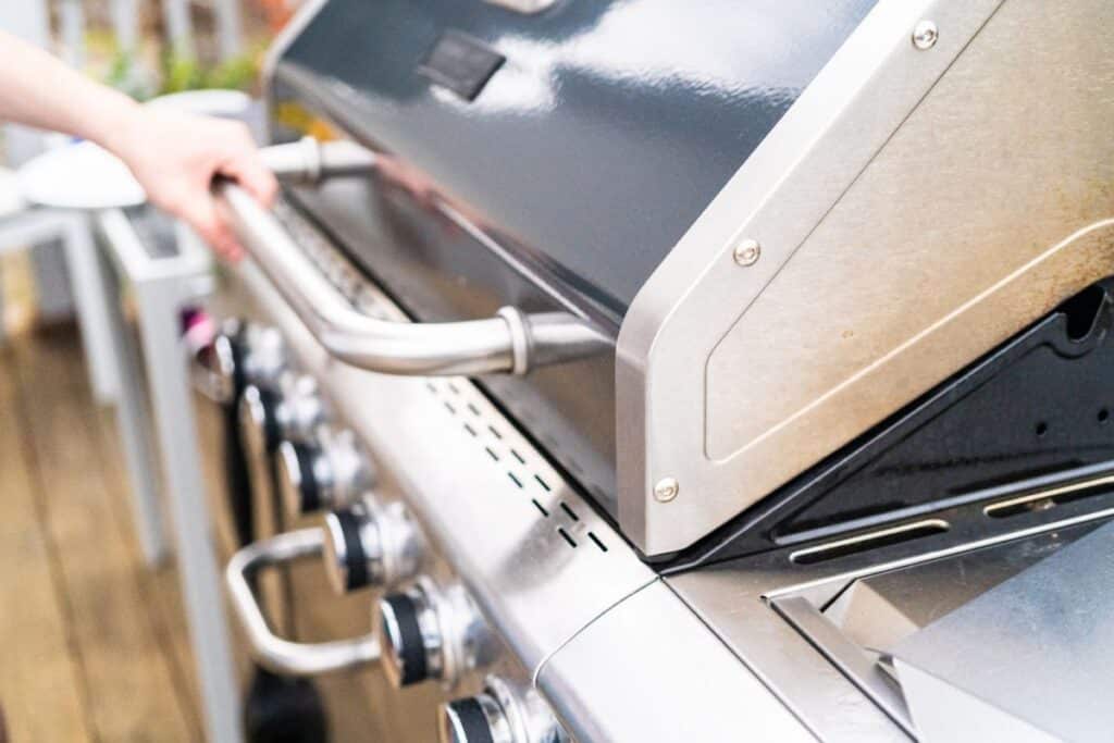 A hand grabs the handle to a natural gas outdoor grill.