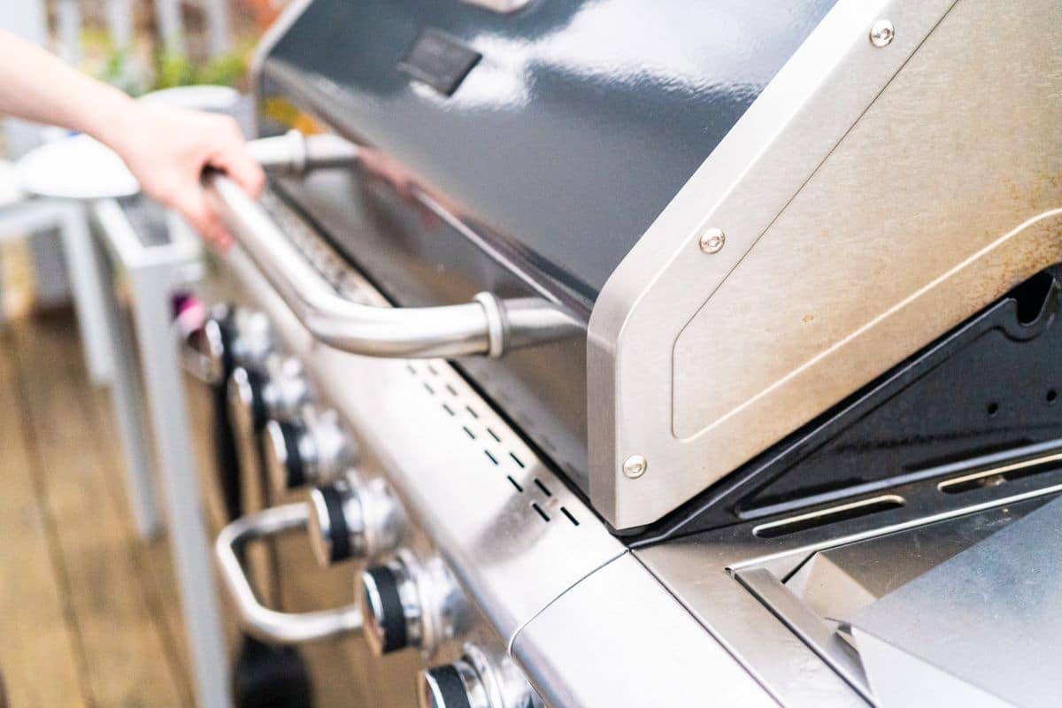 A hand grabs the handle to a natural gas outdoor grill.
