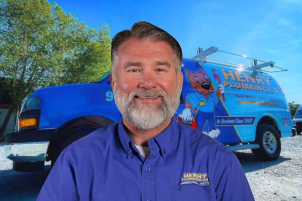 Todd Reed posing in a blue T-shirt branded with Henry Plumbing with the very recognizable Henry Plumbing work truck