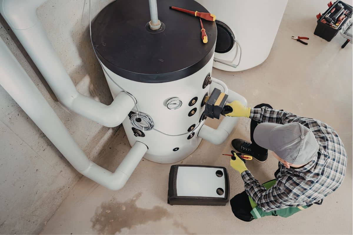 A man kneels next to a water heater performing routine mainenance